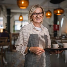 Nice mature woman waitress in apron offer cup of delicious tasty coffee, stand and smile, friendly staff of restaurant (Nice mature woman waitress in apron offer cup of delicious tasty coffee, stand and smile, friendly staff of restaurant, ASCII, 119